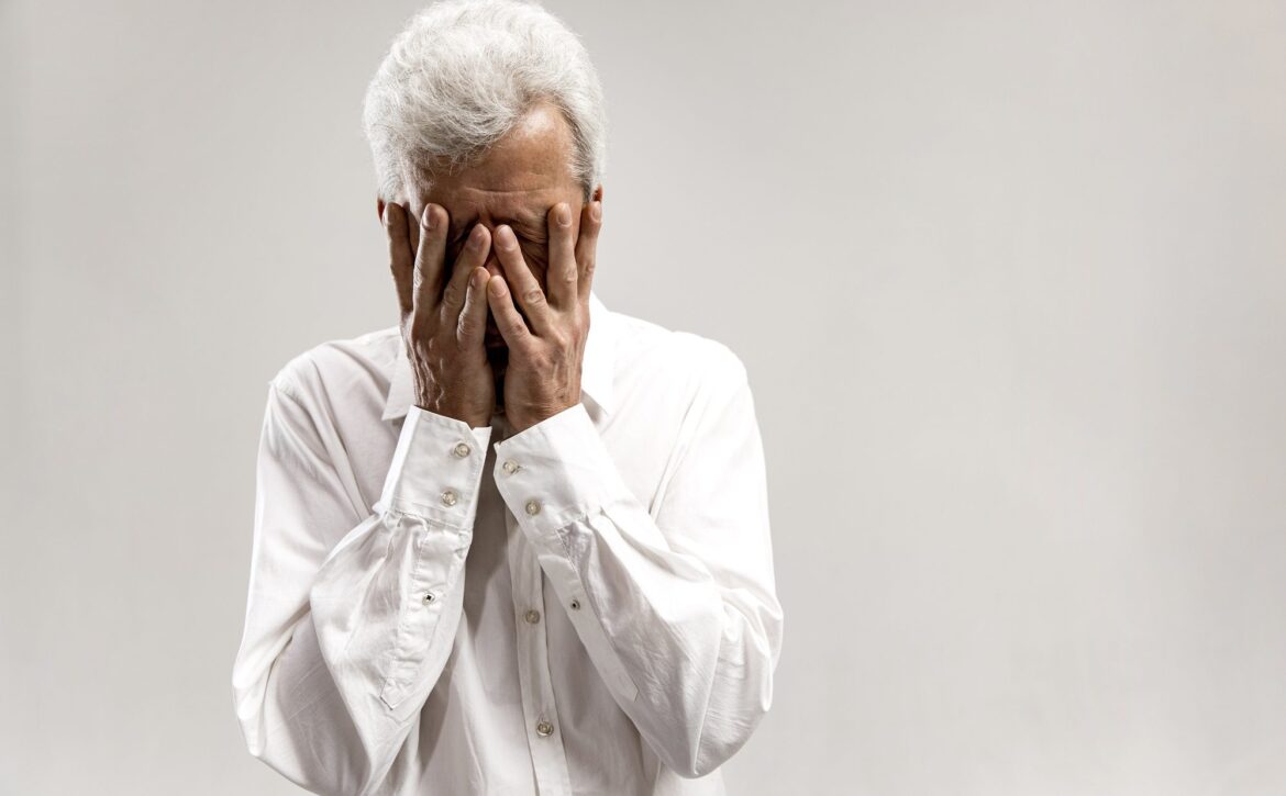 Portrait of upset old man rubbing his eye while crying.